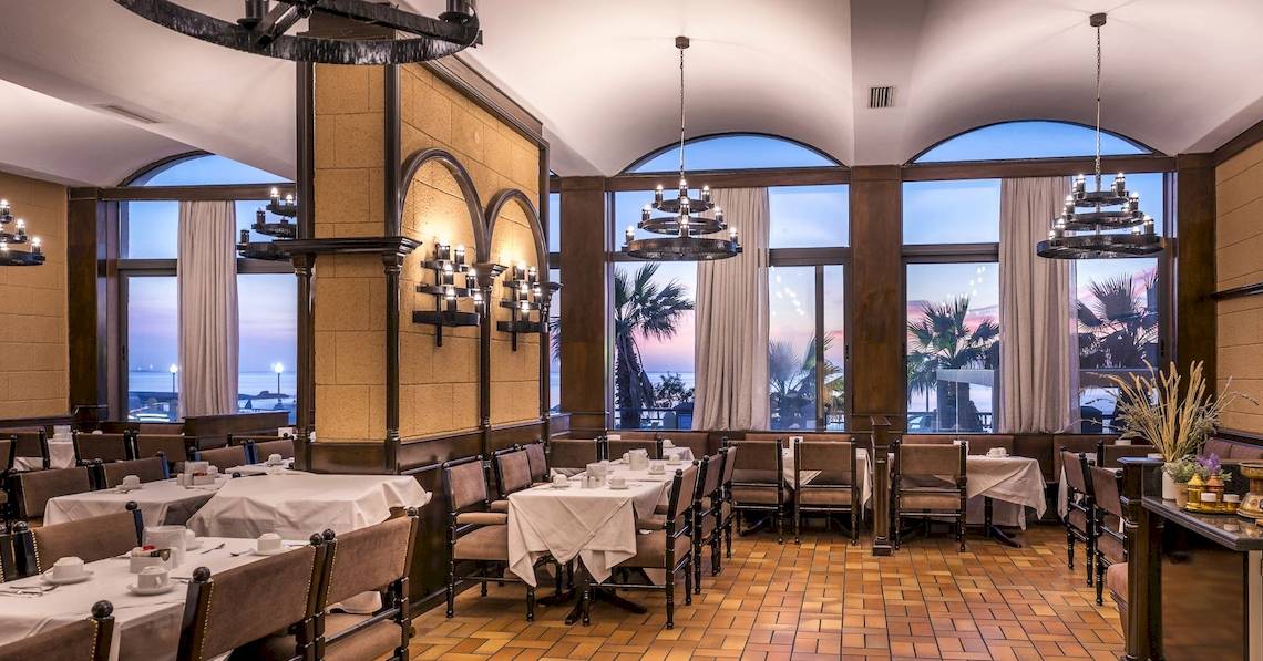 Innenansicht des Restaurants im Mitsis La Vita Beach Hotel mit runden Fenstern und Tischdekoration.