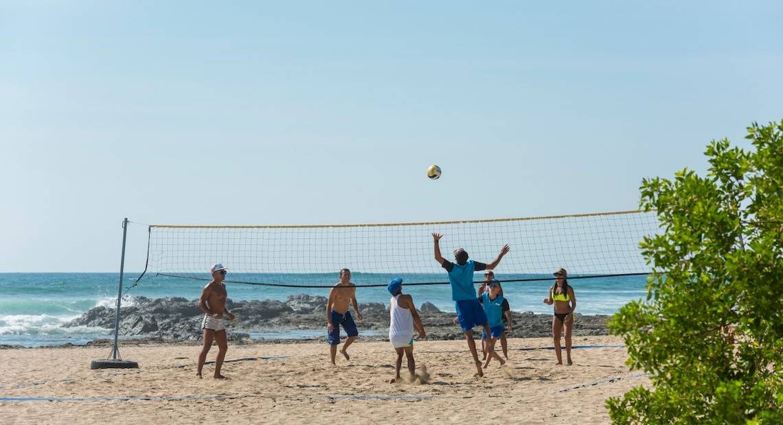Gruppe von Spielern, die Volleyball auf dem Strand vor dem Occidental Tamarindo Hotel spielen.