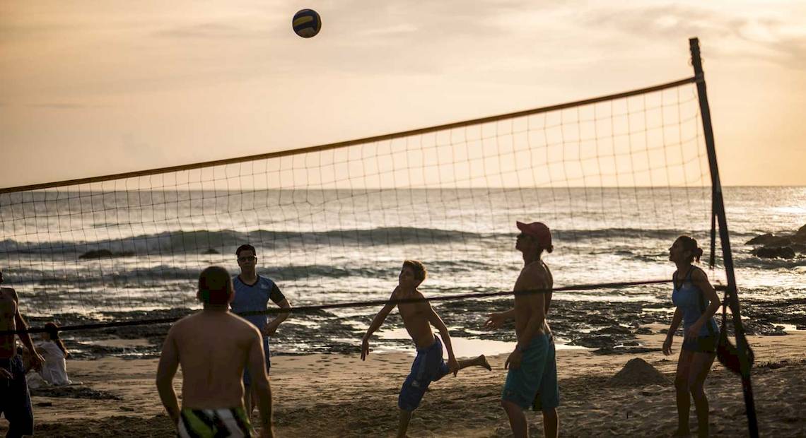 Gruppe von Menschen, die Volleyball auf einem Strand spielen, während die Sonne untergeht.