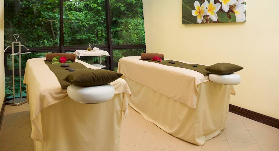 Massage-Behandlungsraum im Hotel Occidental Tamarindo mit Blick auf die Natur, zwei Massageliegen mit Kissen und Steinen.