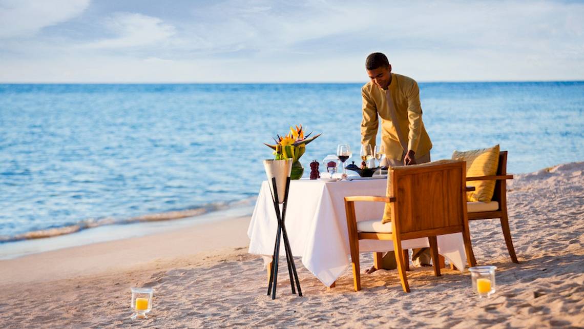 Ein Kellner bereitet ein Essen auf dem Strand am Dhawa Ihuru Hotel vor.