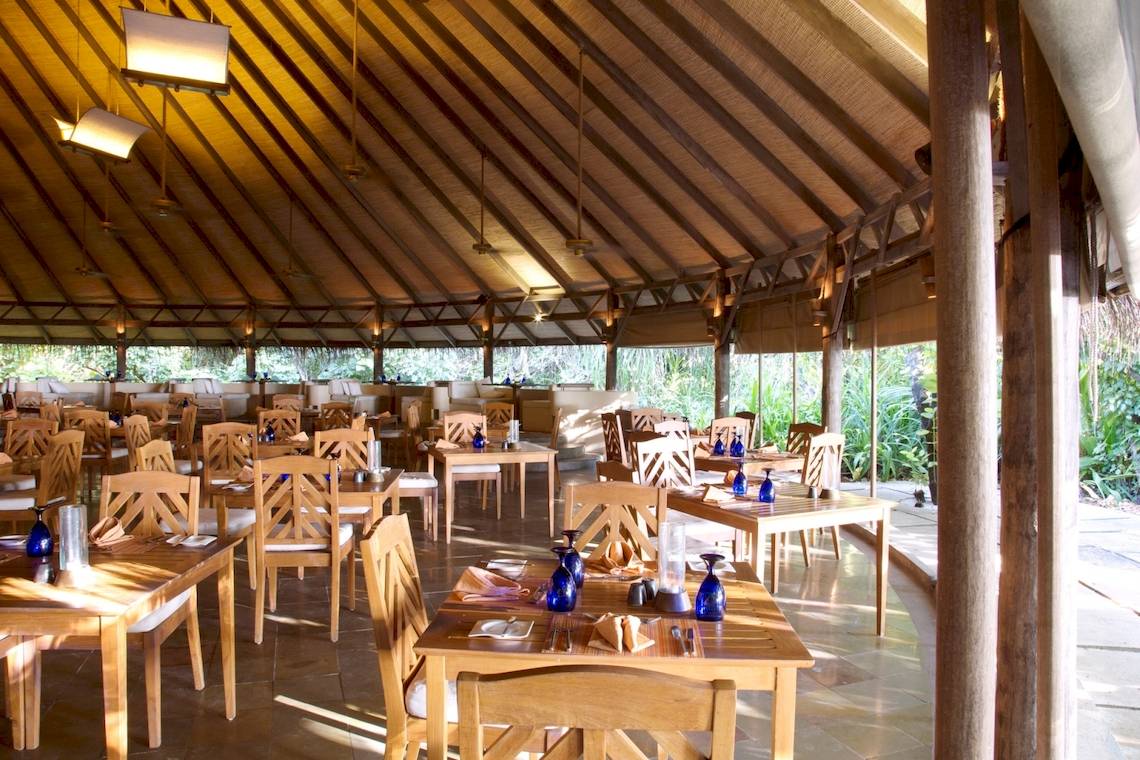 Innenansicht des Coco Palm Dhuni Kolhu Restaurants mit runden Tischen, Stühlen und blauen Gläsern.