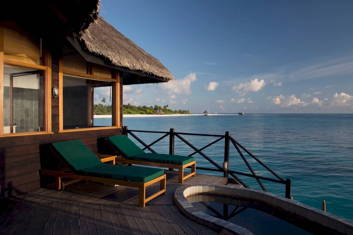 Terrasse des Coco Palm Dhuni Kolhu Hotels mit zwei Liegen und Ausblick auf das Meer.