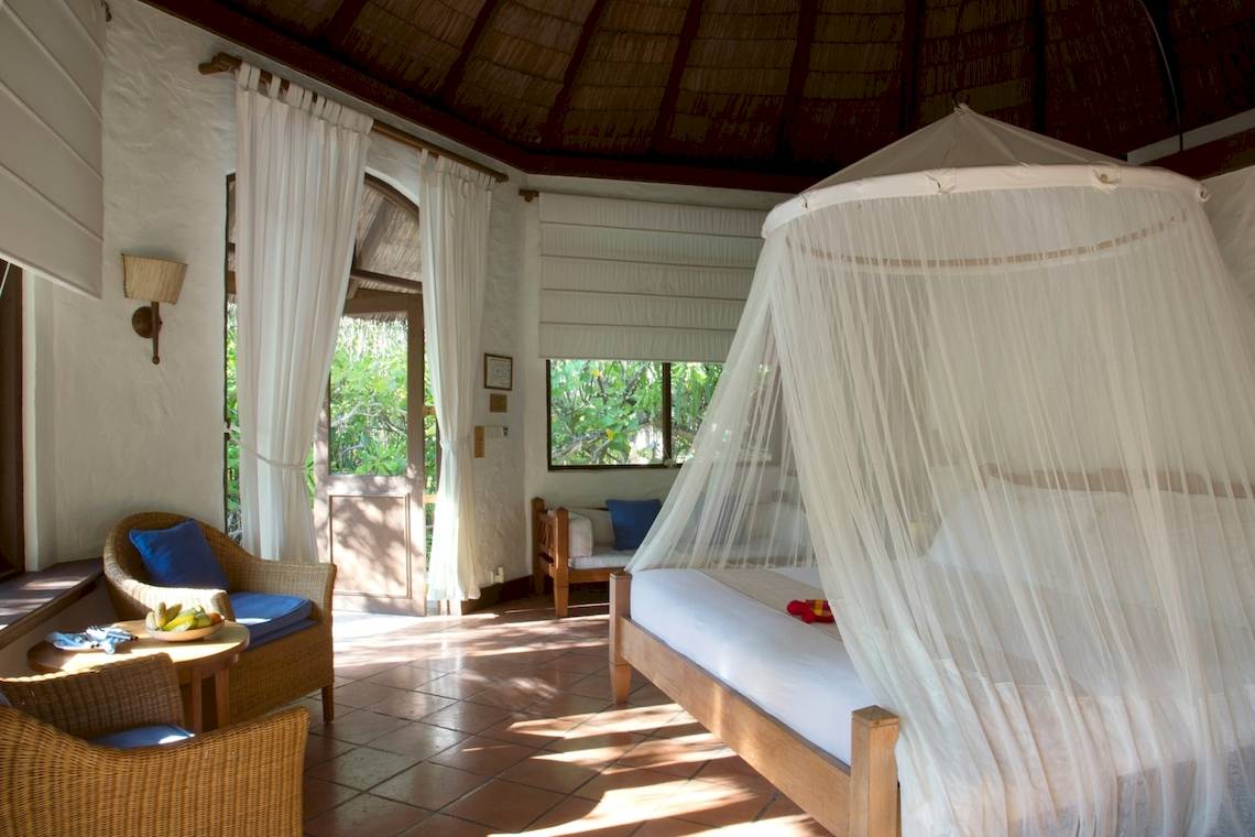 Ein Schlafzimmer im Coco Palm Dhuni Kolhu Hotel mit einem Bett unter einem Moskitonetz und zwei Stühlen.
