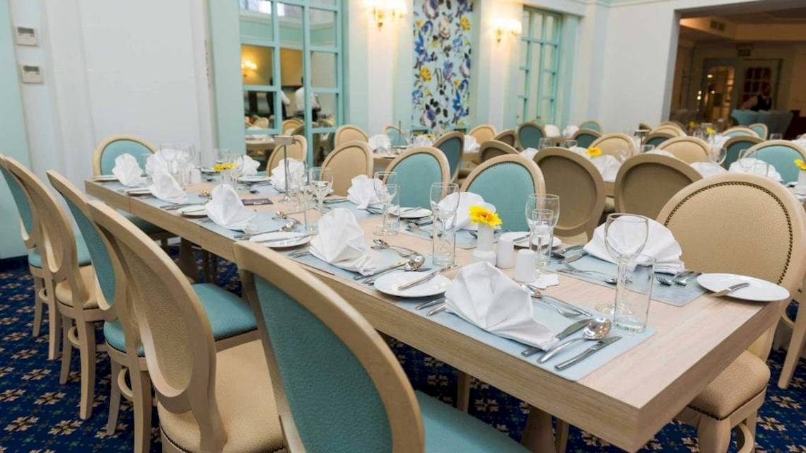 Ein elegantes Esszimmer des AX The Victoria Hotels mit gedeckten Tischen und Stühlen, gelben Blumen und blauen Kissen.