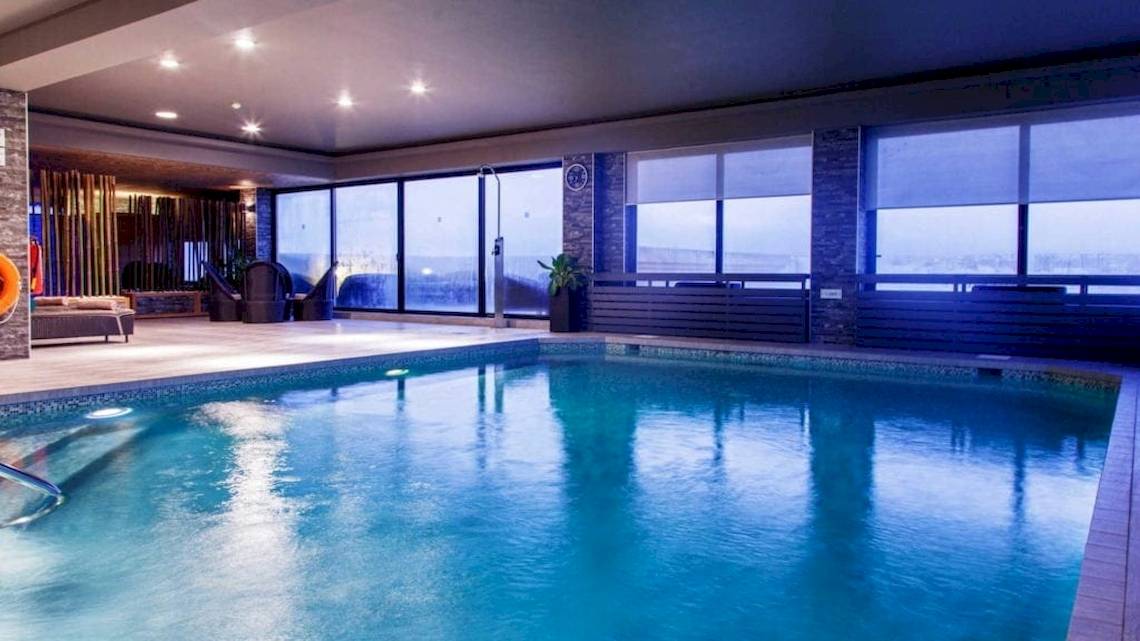 Innenpool im AX The Victoria Hotel mit großen Fenstern und Ausblick auf die Stadt.