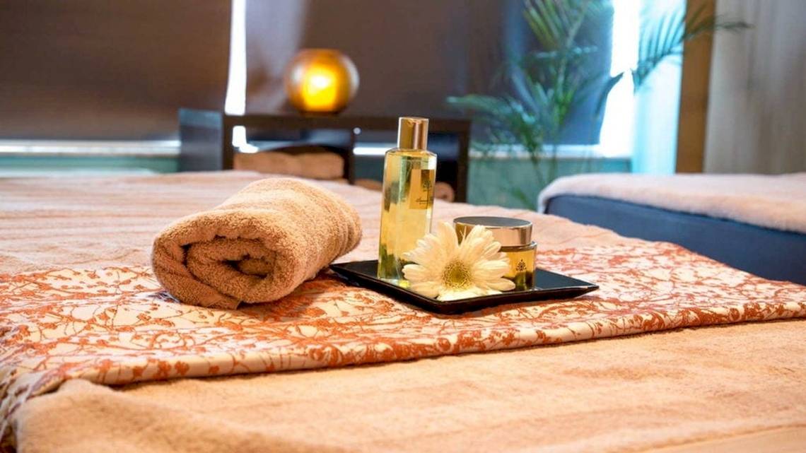 Spa-Behandlungsbereich im AX The Victoria Hotel mit einem Bett, Handtüchern, Blumen und Pflegeprodukten.