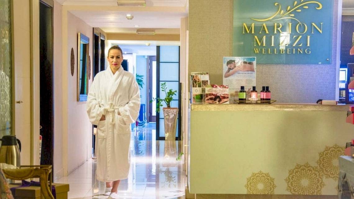 Eine Frau in einem weißen Bademantel steht vor dem Empfangsbereich von Marion Mizzi Wellbeing.