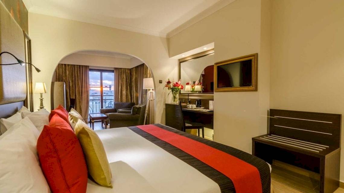 Zimmer im AX The Victoria Hotel mit Bett, Kissen, Schreibtisch, Sessel, Lampe und Balkon