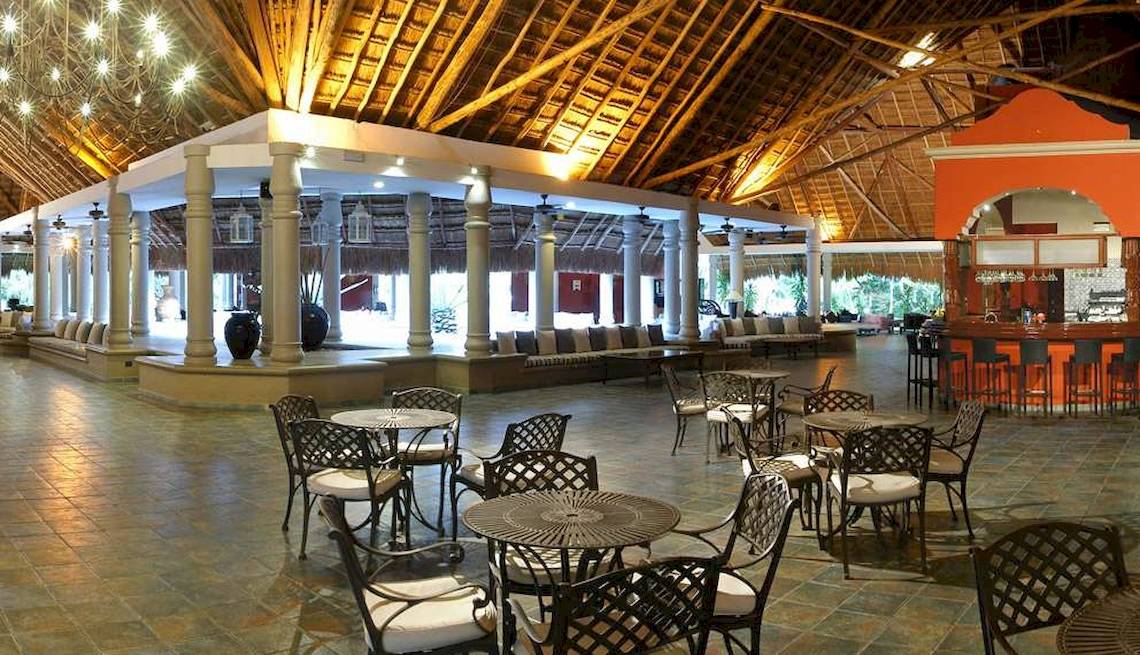 Hotellobby des Catalonia Playa Maroma mit Tischen, Stühlen und einer Bar.