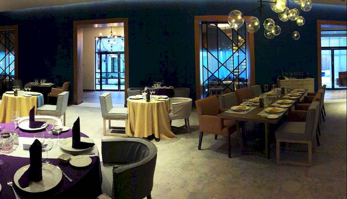 Innenansicht des Restaurants im Catalonia Playa Maroma Hotel mit gedeckten Tischen und dekorativen Kronleuchtern.
