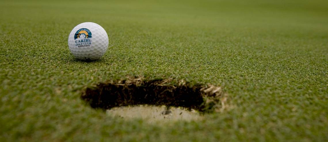 Ein Golfball mit dem Logo Caribe Golf Club liegt auf einem Golfplatz neben einem Loch.
