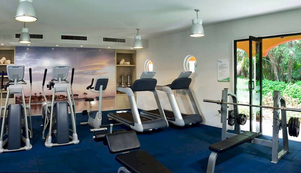 Fitnessstudio im Catalonia Playa Maroma Hotel mit Laufbändern, Kraftgeräten und Blick aufs Meer.