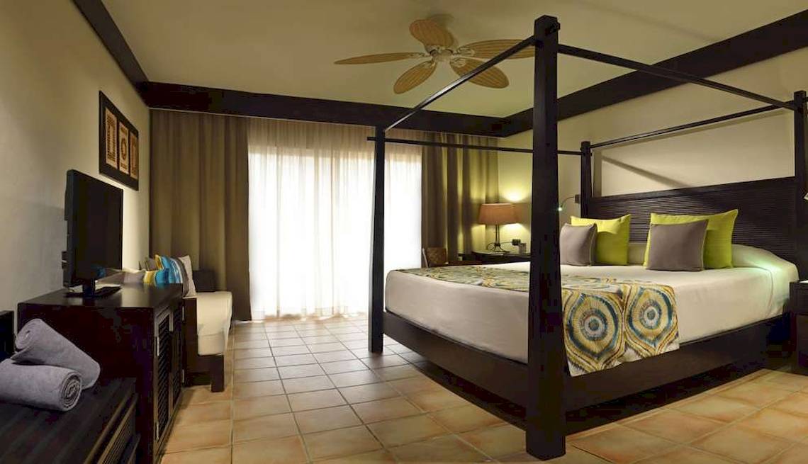 Hotelzimmer im Catalonia Playa Maroma mit Himmelbett, Fernseher, und luxuriöser Einrichtung.
