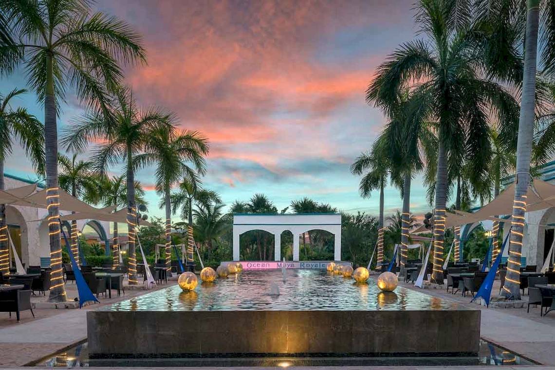 Gartenbereich des Ocean Maya Royale Hotels bei Sonnenuntergang mit Brunnen und Palmen