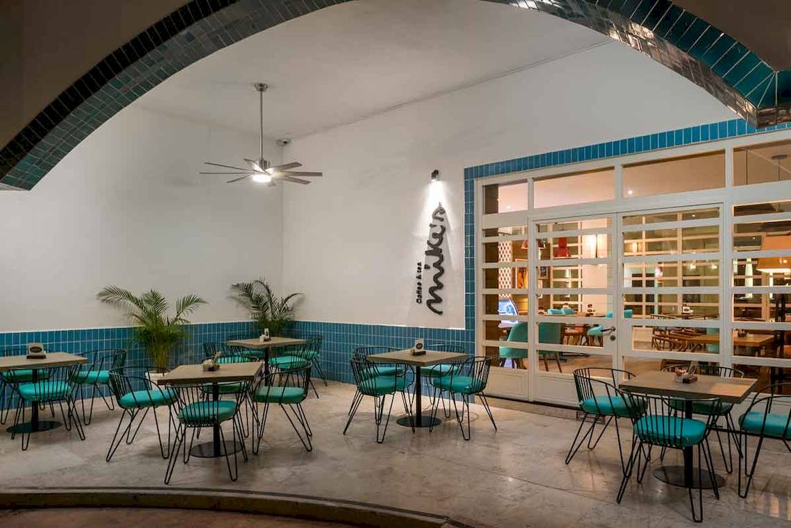 Innenbereich des Ocean Maya Royale Hotels mit grünen Tischen und Stühlen, blauen Fliesen und einer Decke mit Ventilator.
