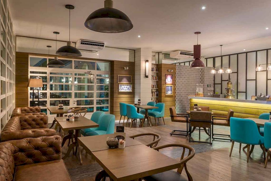 Innenbereich des Ocean Maya Royale Hotels mit modernen Möbeln, blauen Stühlen, Holztischen und einer Bar.