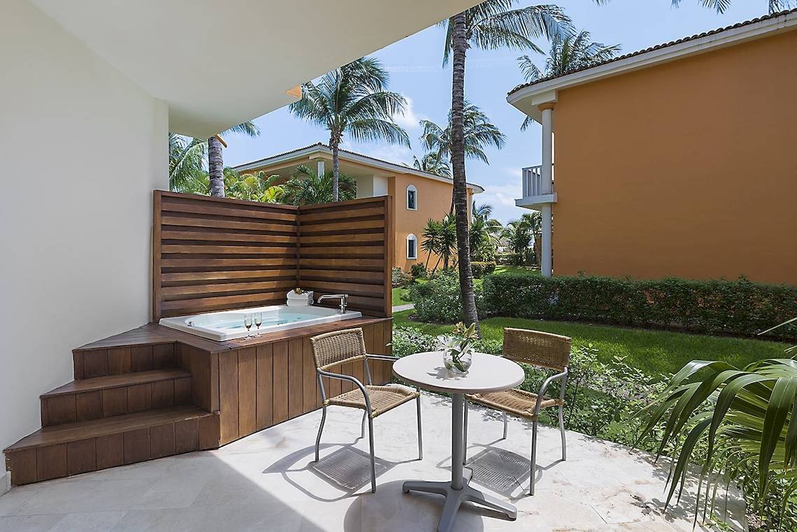 Terrasse des Ocean Maya Royale Hotels mit Jacuzzi und Tisch, umgeben von Gärten und Gebäuden.