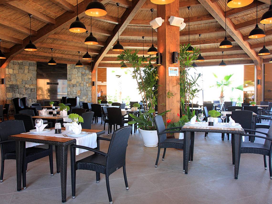 Innenbereich des Restaurants im Wyndham Residences Kusadasi Golf & Spa mit Tischen, Stühlen und Pflanzen.
