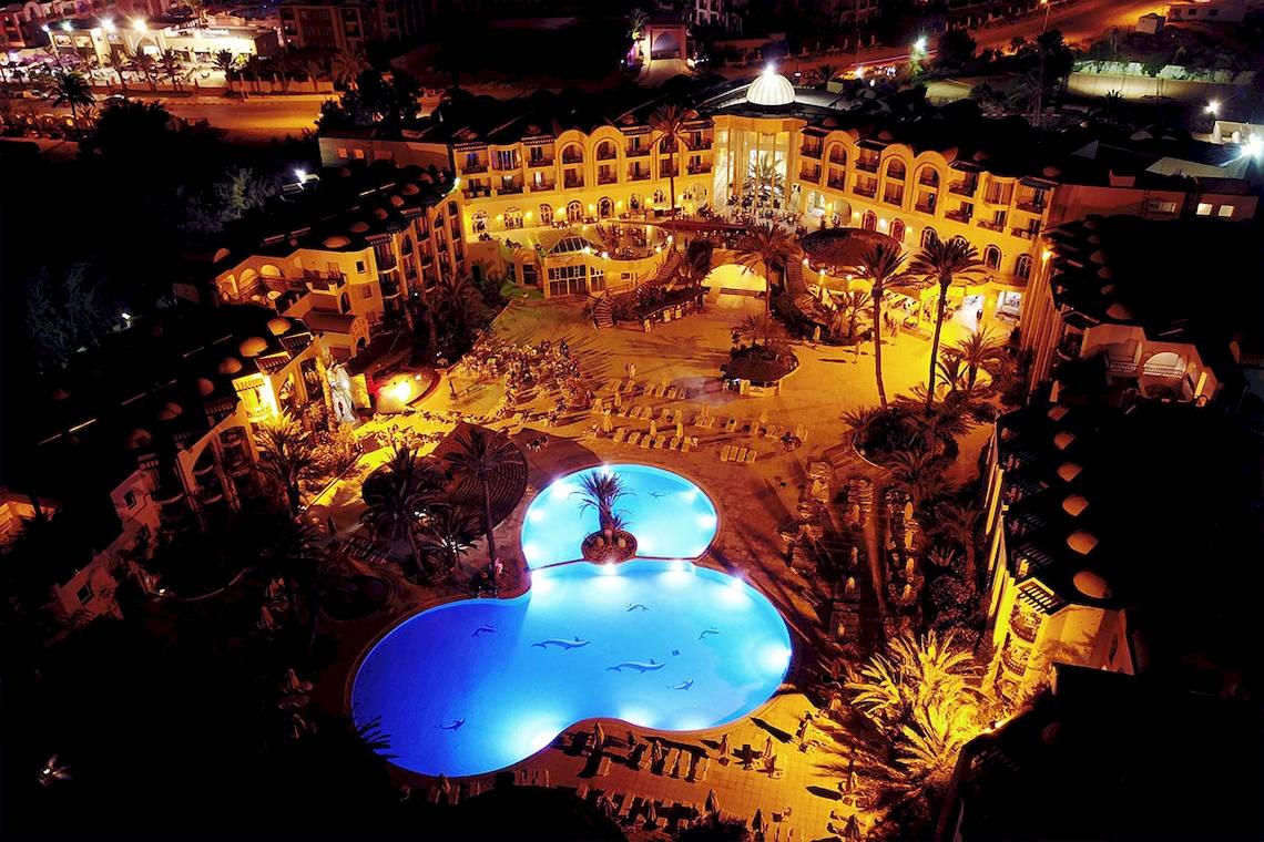 Eine abendliche Luftaufnahme des Eden Star Zarzis Hotels mit einem großen Pool und beleuchteten Gebäuden.