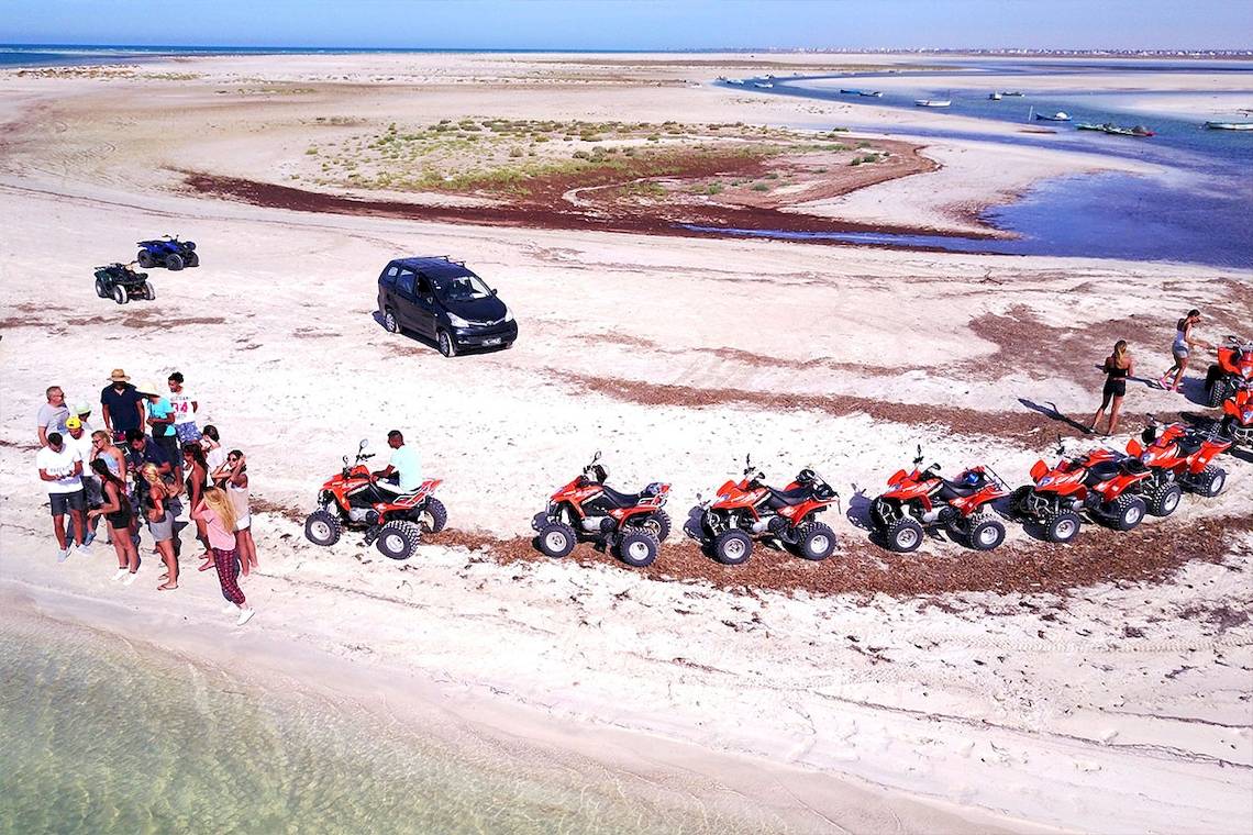 Gruppe von Menschen am Strand neben roten Quads und einem schwarzen Auto bei Eden Star Zarzis