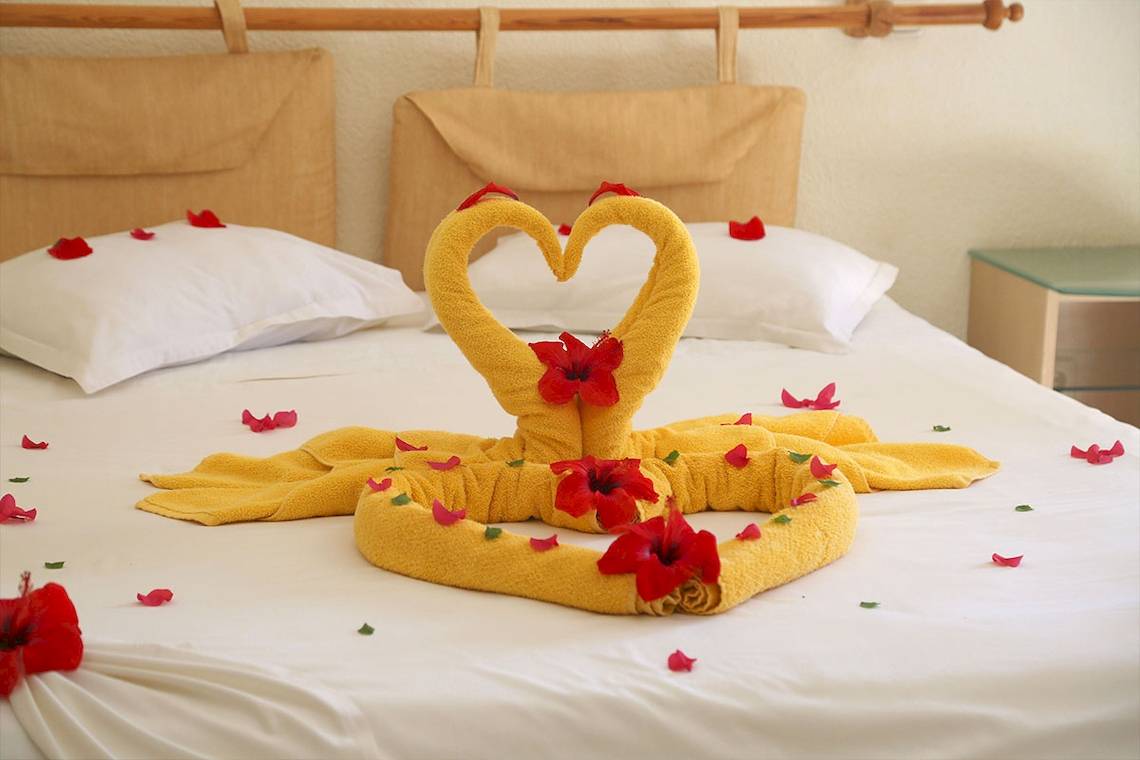 Ein Bett mit einem Herz-förmigen Handtuch-Arrangement und roten Blumen.