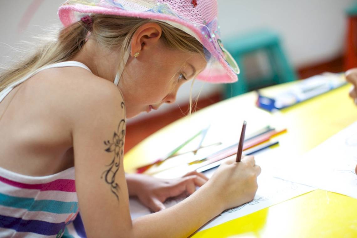 Ein Madchen mit einem Tattoo am Arm zeichnet auf einem gelben Tisch.