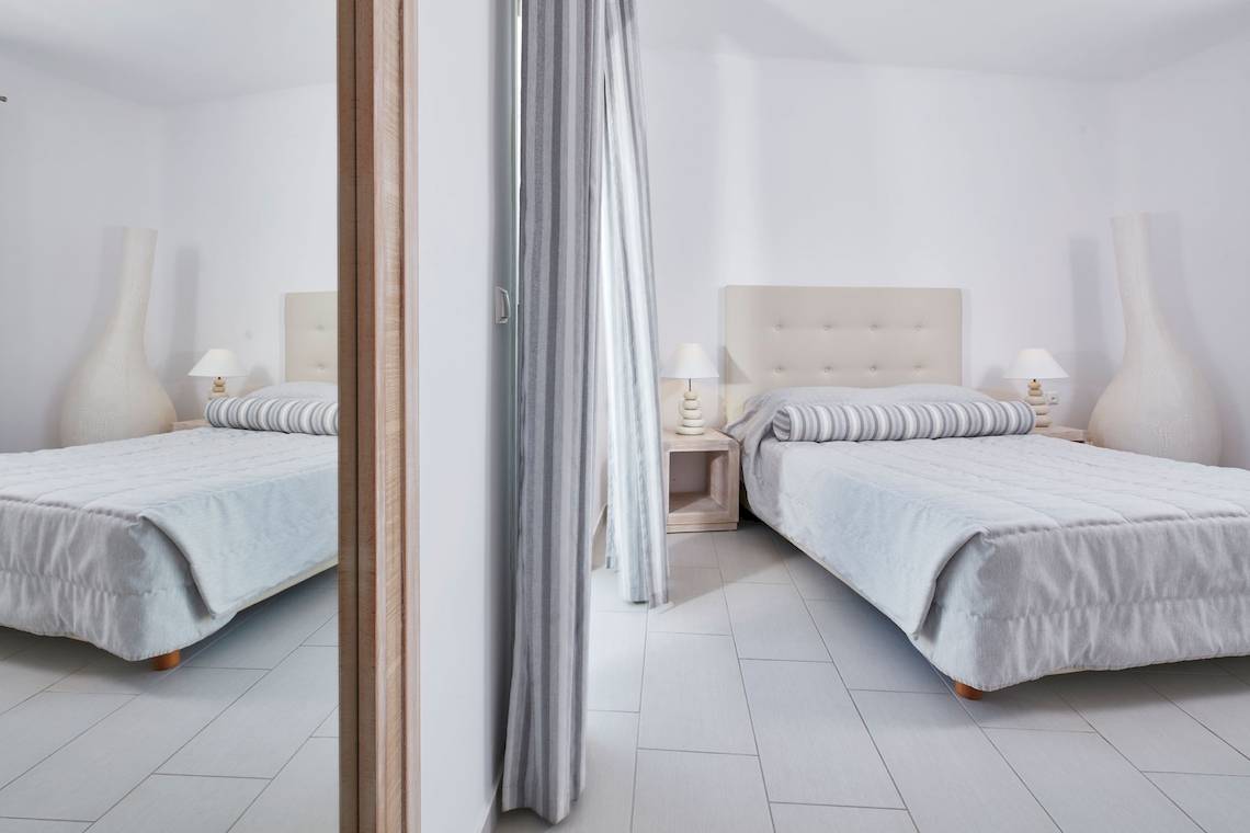 Zwei Schlafzimmer im Aegean Plaza Hotel mit weißen Möbeln und grauen Vorhängen.