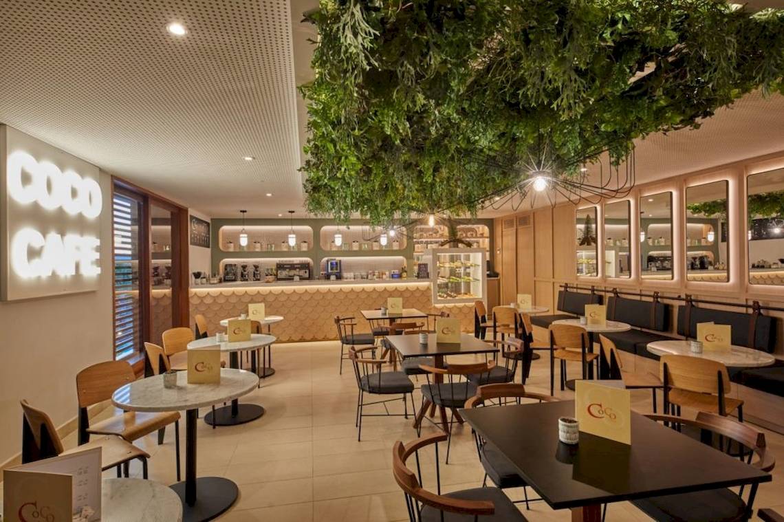 Innenansicht des Coco Cafe mit grünen Pflanzen und runden Tischen und Stühlen