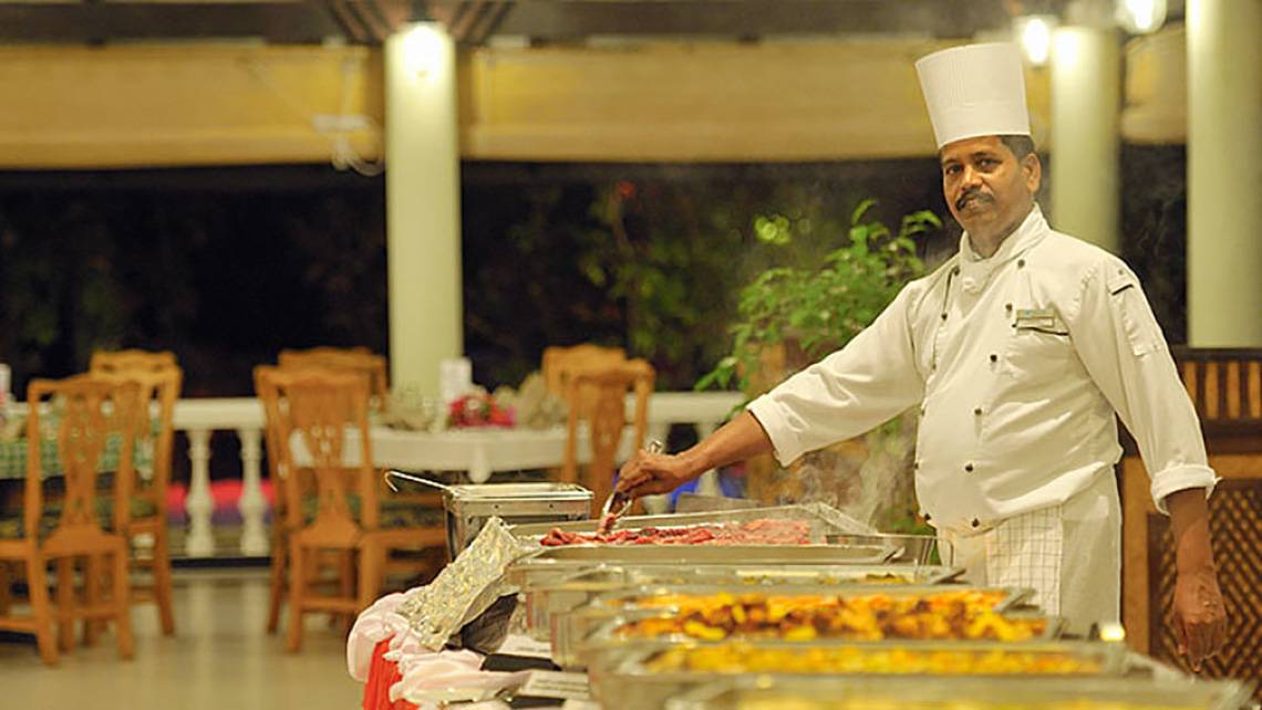 Koch in weißer Uniform bereitet Speisen auf einem Buffet im Holiday Island Resort & Spa zu.