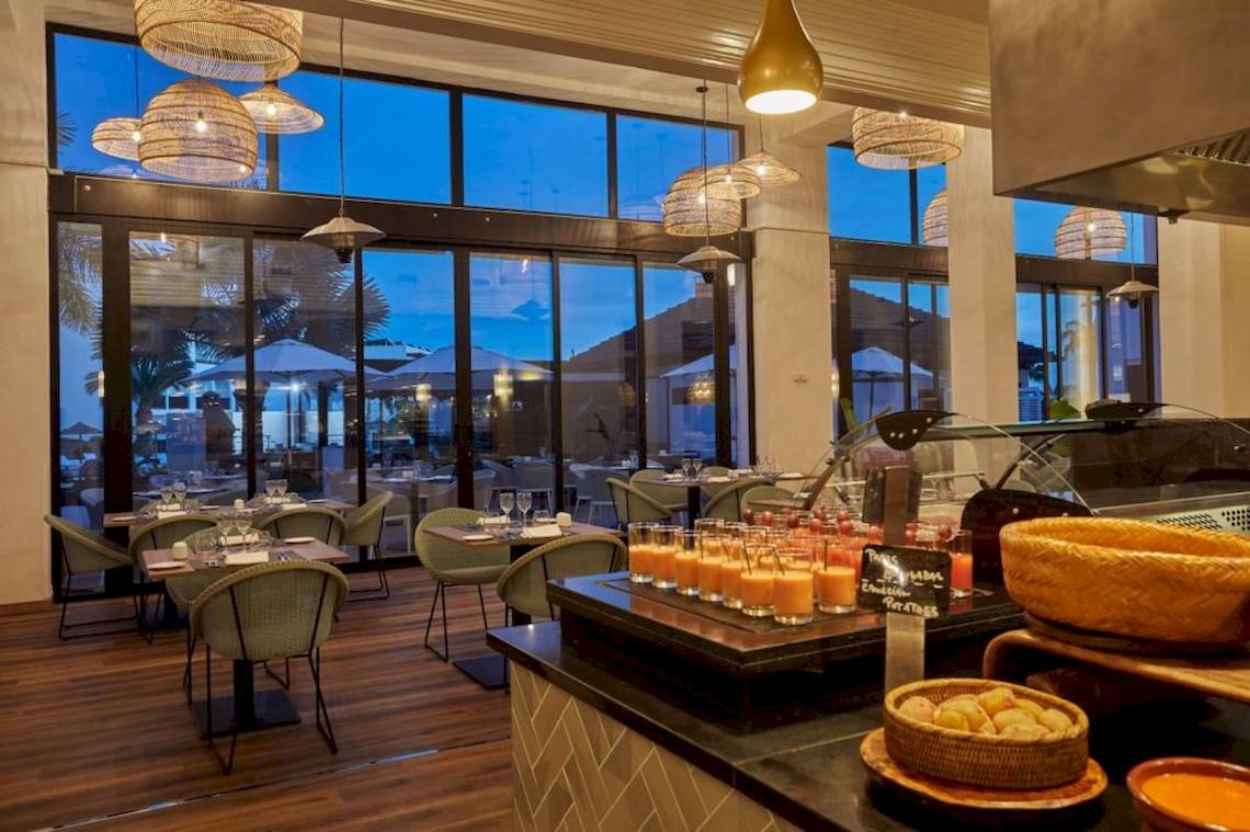 Innenansicht des Restaurants im Secrets Lanzarote Resort & Spa mit Tischen, Stühlen und Aussicht auf den Außenbereich.
