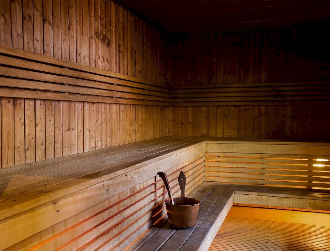 Sauna im Radisson Blu Hotel & Resort, Abu Dhabi mit Holzwänden, Bänken und einem Eimer auf der Bank.