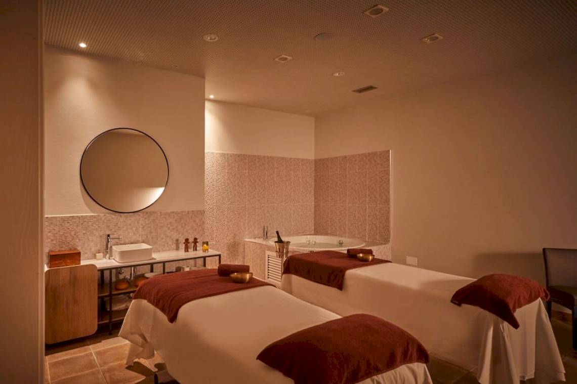 Ein Spa-Behandlungsraum mit zwei Massagetischen, einer Badewanne und einem Spiegel.