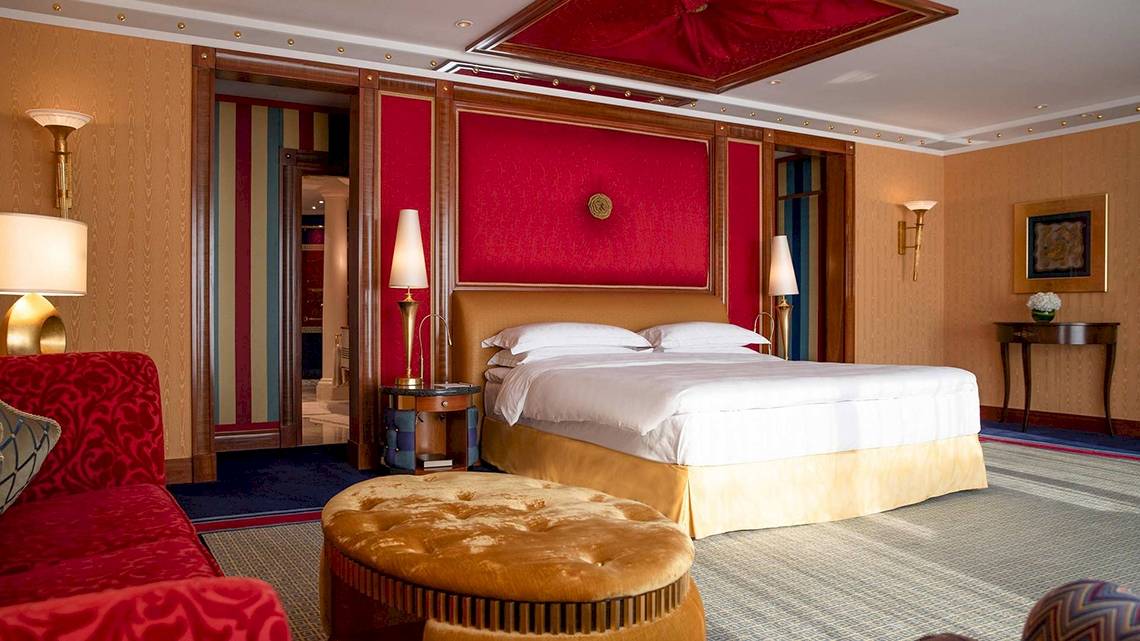 Schlafzimmer im Burj Al Arab Jumeirah Hotel mit rotem Wanddesign, goldenem Bett und zwei Nachttischen.