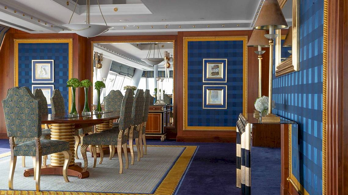 Speisesaal im Burj Al Arab Jumeirah mit blauen Wänden, goldenen Akzenten und einem runden Tisch mit Stühlen.