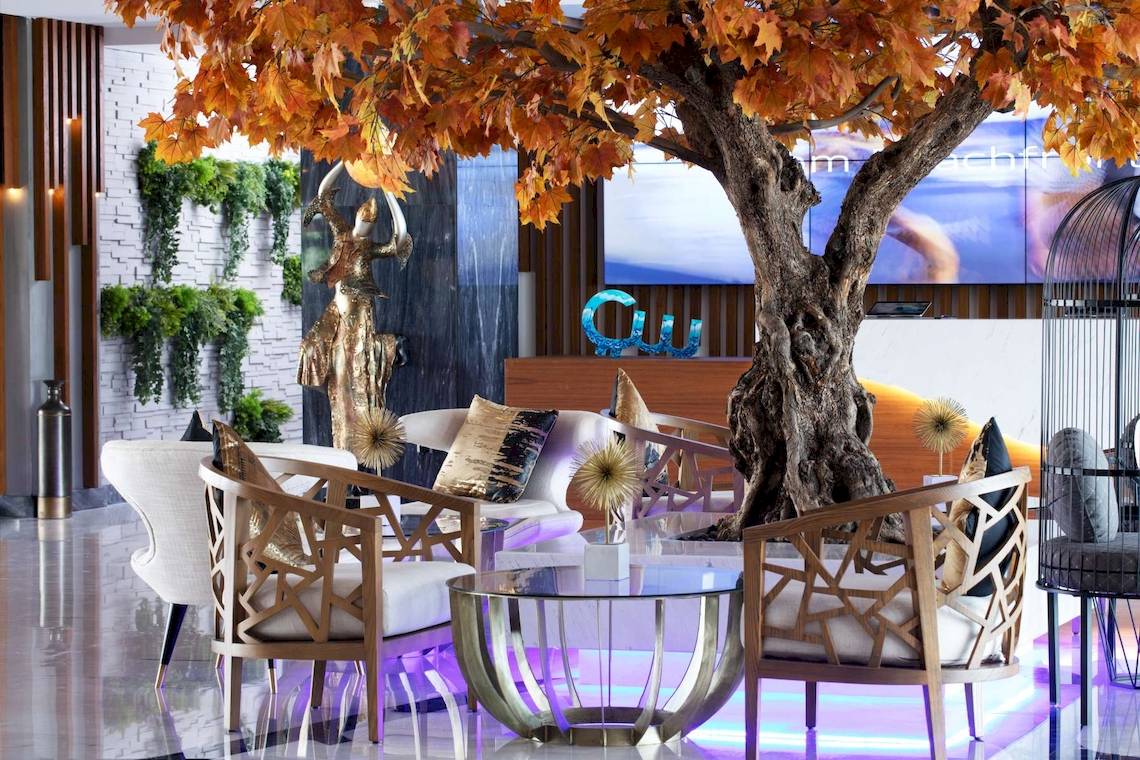 Lobby des C Central Hotel & Resort The Palm mit zentralem Baum, Sofas und goldener Statue.