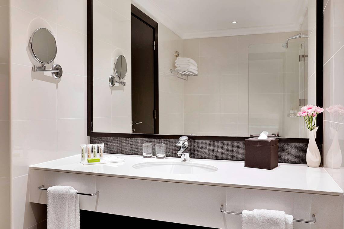 Badezimmer im Le Meridien Mina Seyahi Beach Resort mit weißem Waschbecken und Spiegel.
