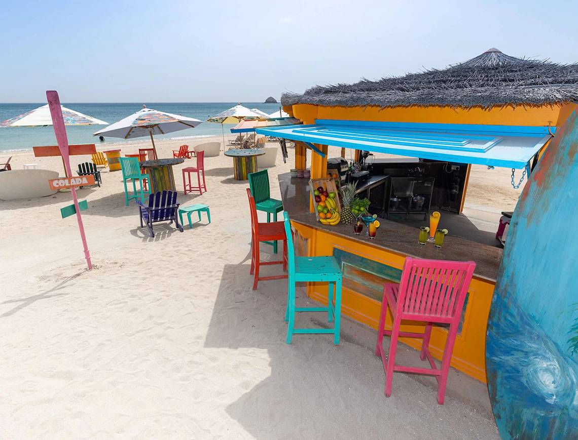 Strandbar im Radisson Blu Resort, Fujairah, mit bunten Stühlen und Tischen.