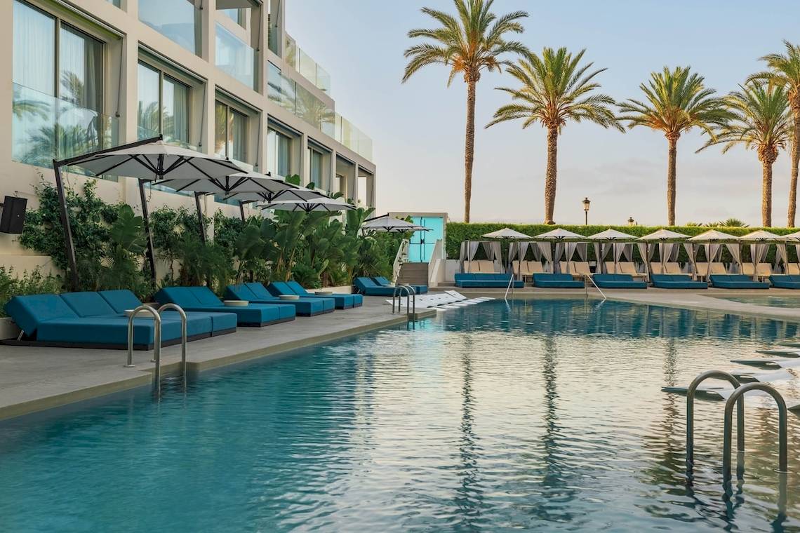 Außenpool des W Ibiza Hotels mit blauen Liegen und Sonnenschirmen