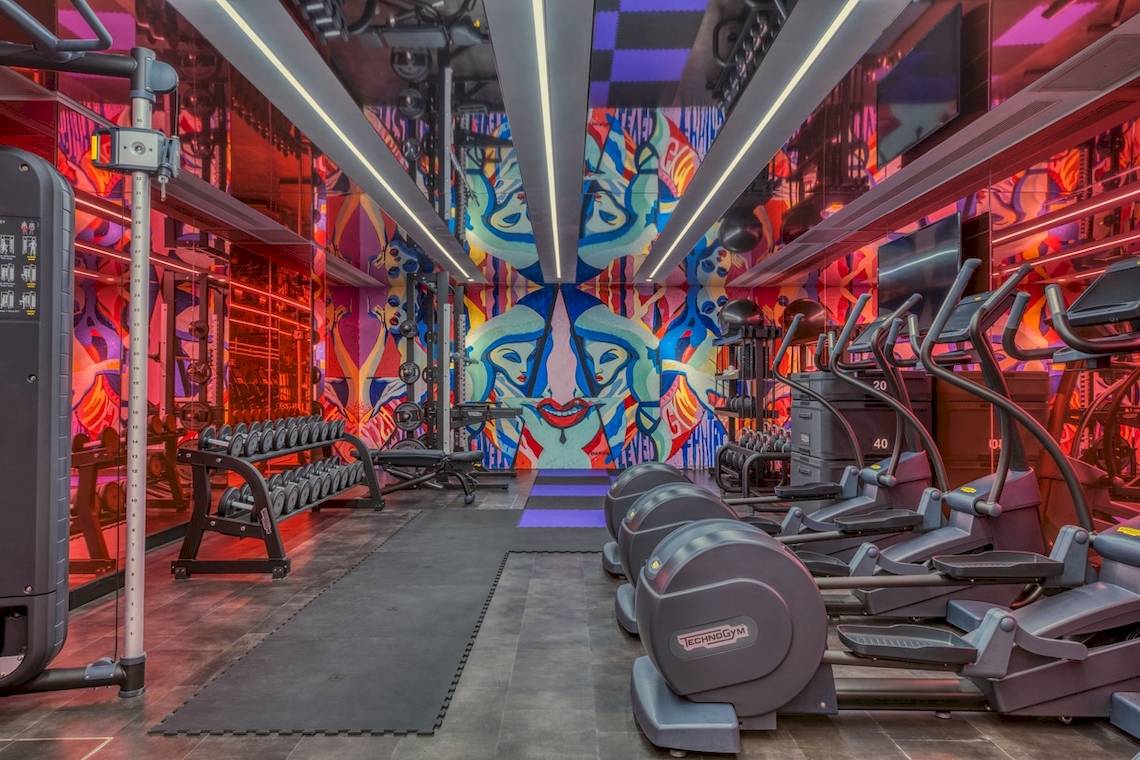 Fitnessstudio im W Ibiza Hotel mit bunten Wänden und Technogym-Geräten.
