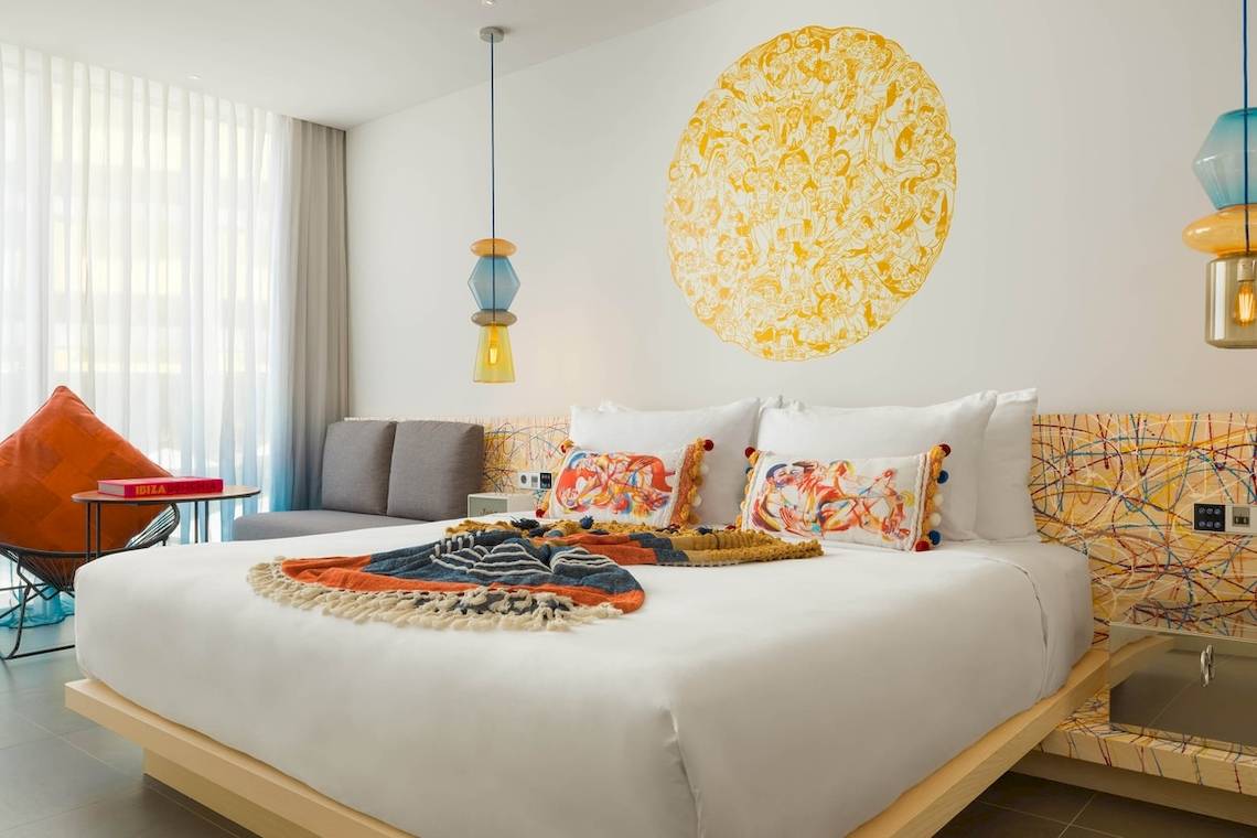 Schlafzimmer im W Ibiza Hotel mit bunten Wanddekorationen und einem Bett.