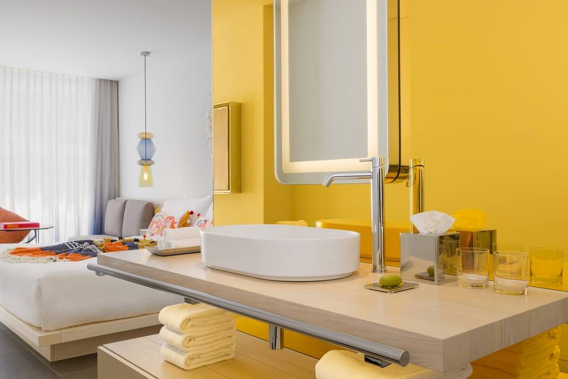Badezimmer im W Ibiza Hotel mit gelben Wänden, Waschbecken, Spiegel und Toilettenartikeln.