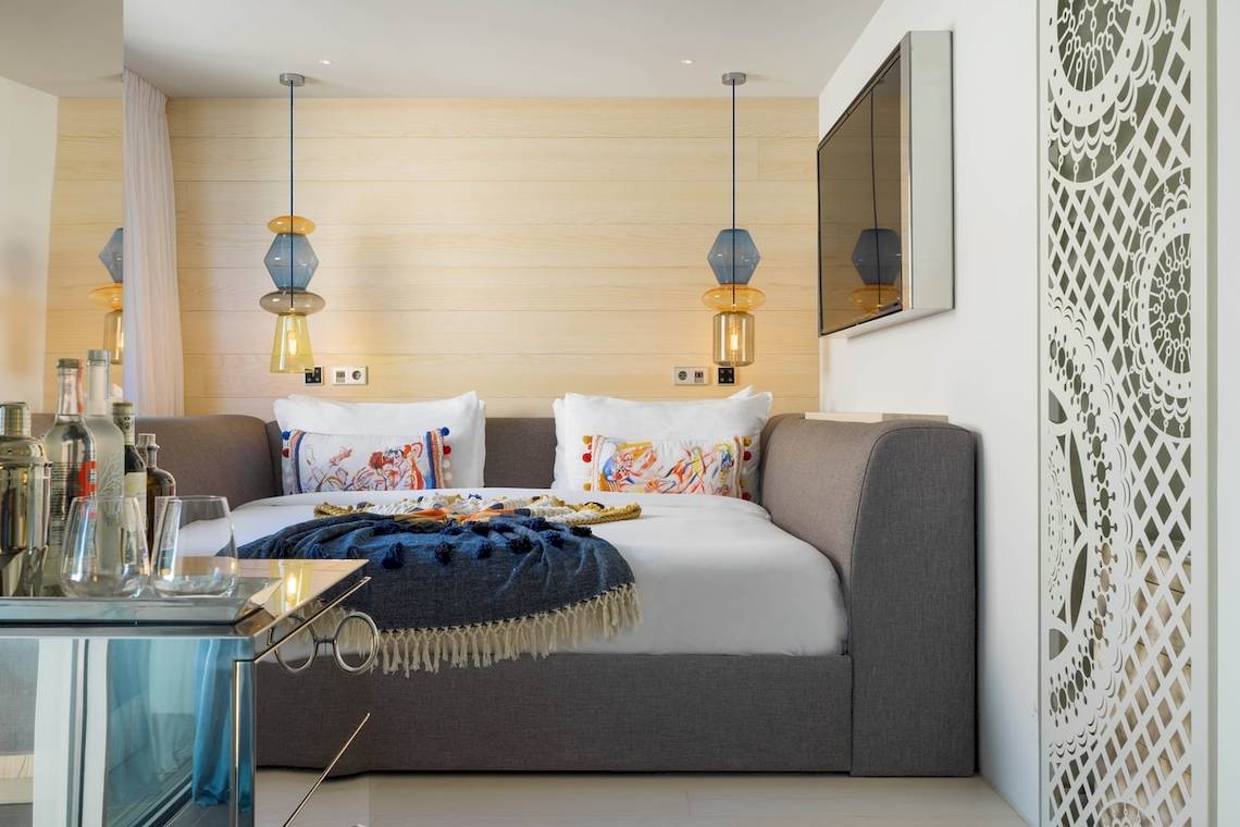 Inneneinrichtung des Schlafzimmers im W Ibiza Hotel mit Bett, Kissen, Decken, Lampen und Fernseher.