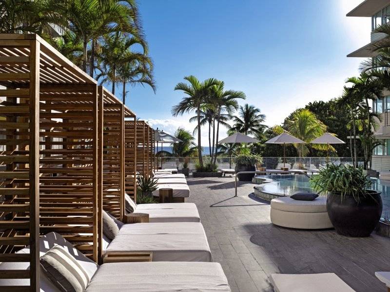 Loungebereich des Victor South Beach Hotels mit Pool, weißen Liegen und Palmen.