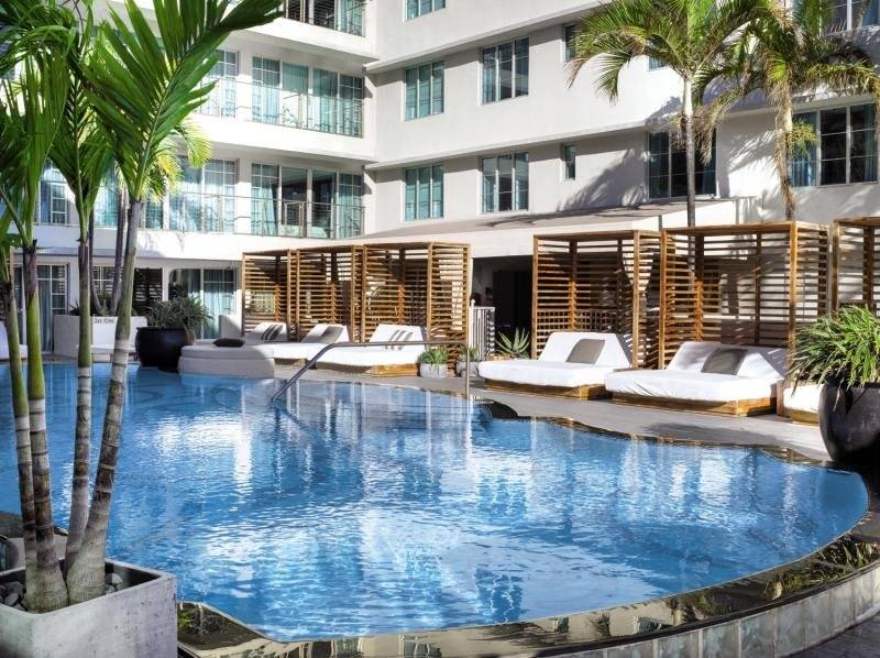 Pool-Lounge-Bereich des Victor South Beach Hotels mit weißen Sonnenliegen und braunen Holzschirmen.