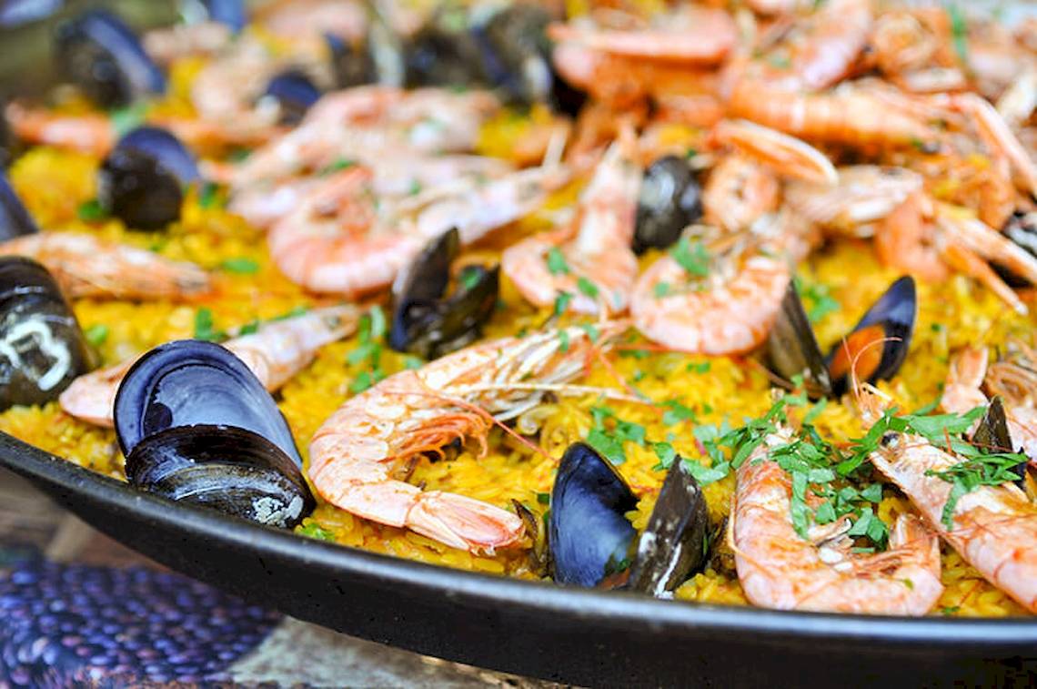 Eine große Platte Paella mit Garnelen und Muscheln, serviert auf einem runden Tisch.