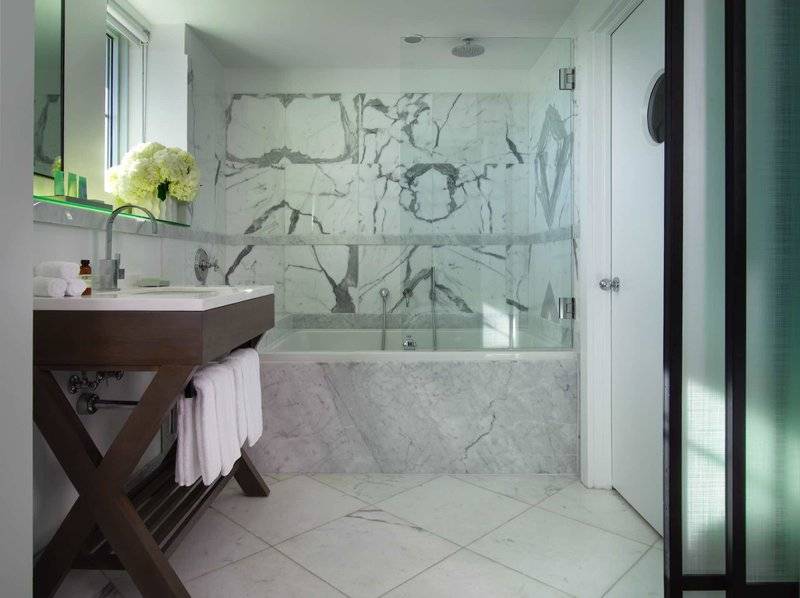 Badezimmer im Victor South Beach Hotel mit Marmorwänden, Badewanne und modernem Waschtisch.
