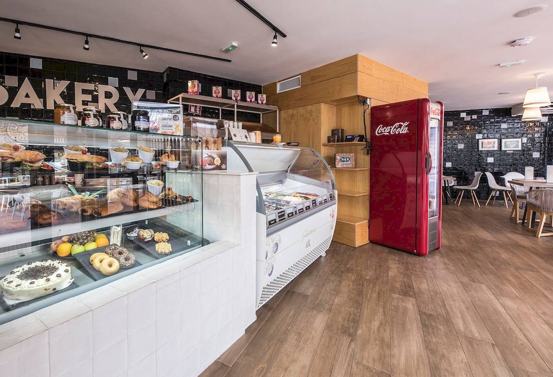 Innenansicht einer Bäckerei mit Kuchendisplay, Getränkeautomat und Essbereich.