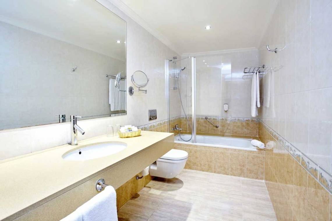 Badezimmer im Laguna Hotel mit Spiegel, Waschbecken, Toilette und Badewanne.