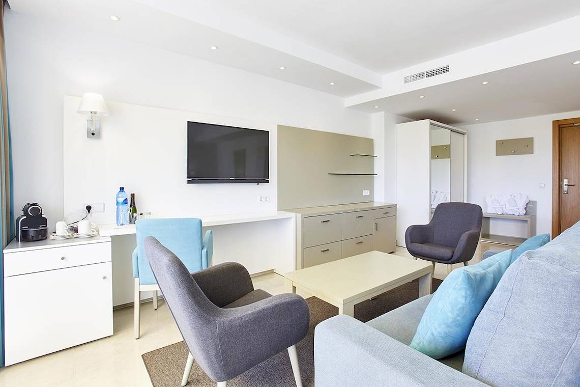 Wohnbereich im Lido Park Hotel mit Fernseher, Schreibtisch, Stühlen und Sofa.